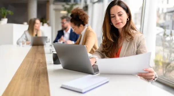 Eine Frau blickt in einem sonnenbelichtetem Konferenzzimmer fokussiert auf ein Formular.